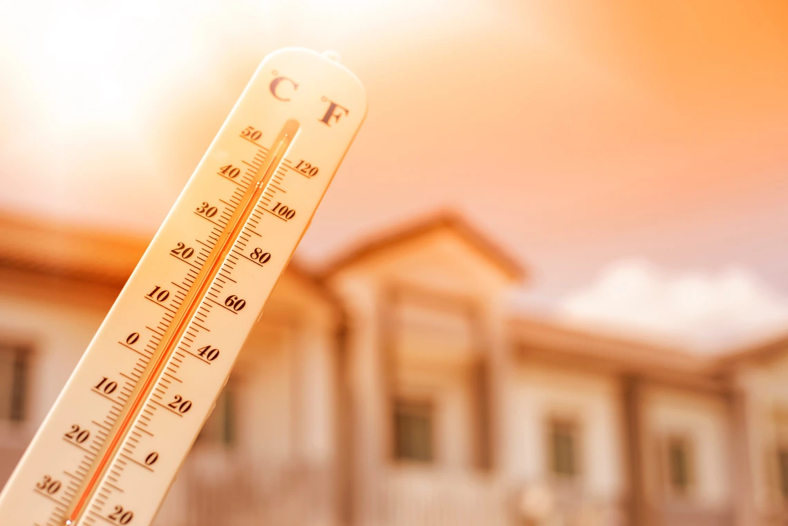 A thermometer held in the sun with a building in the background.